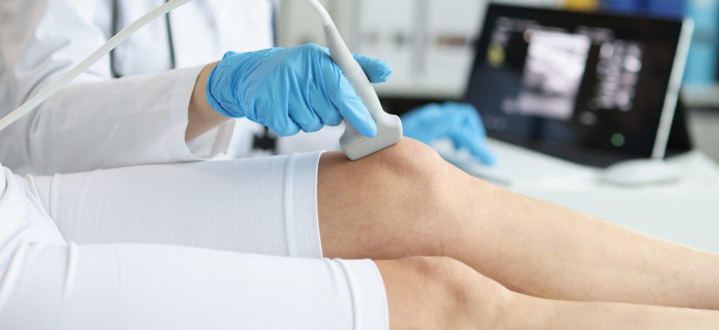 Orthopedic doctor makes ultrasound examination of tpatient knee in clinic