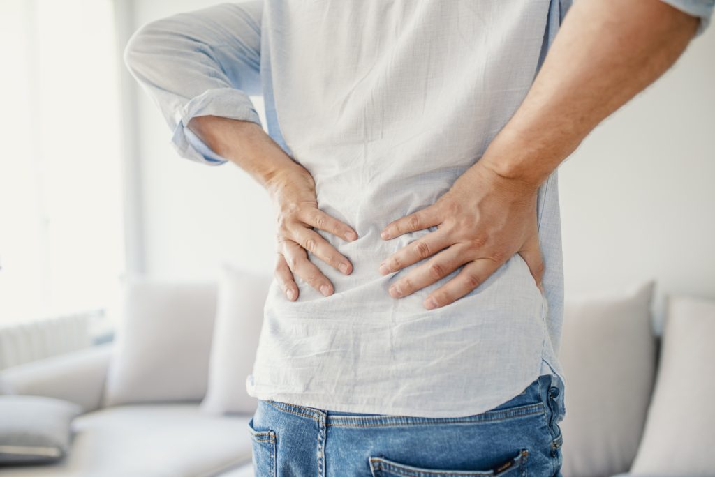 Unhappy senior man suffering from pain in back or reins at home